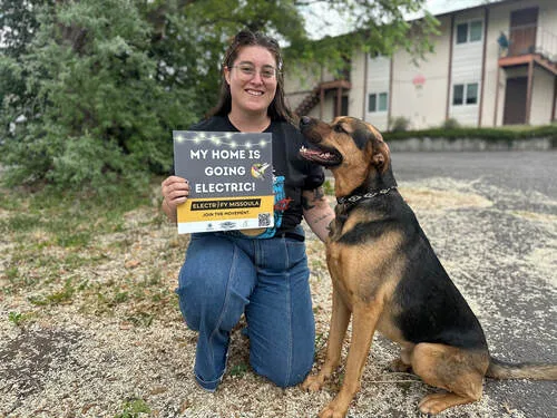 Photograph of a young womain and her dog holding a sign that says 